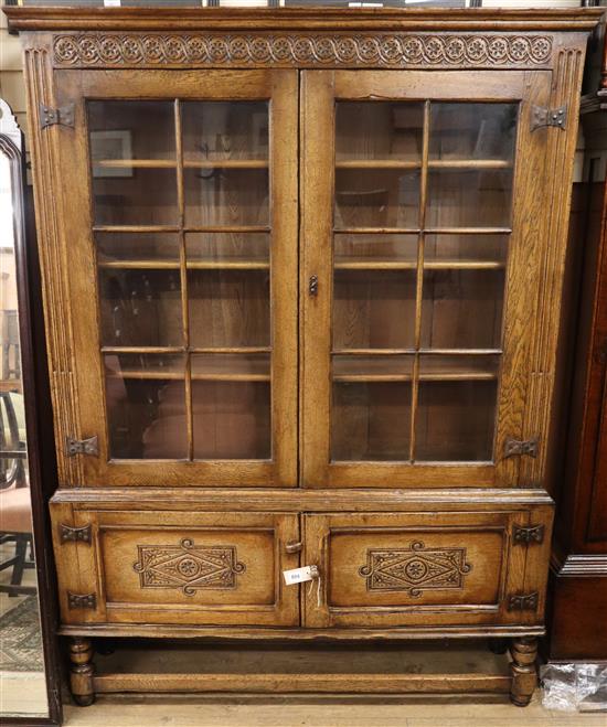 A reproduction carved and panelled oak bookcase, fitted astragal-glazed doors on stretcher base W.130cm